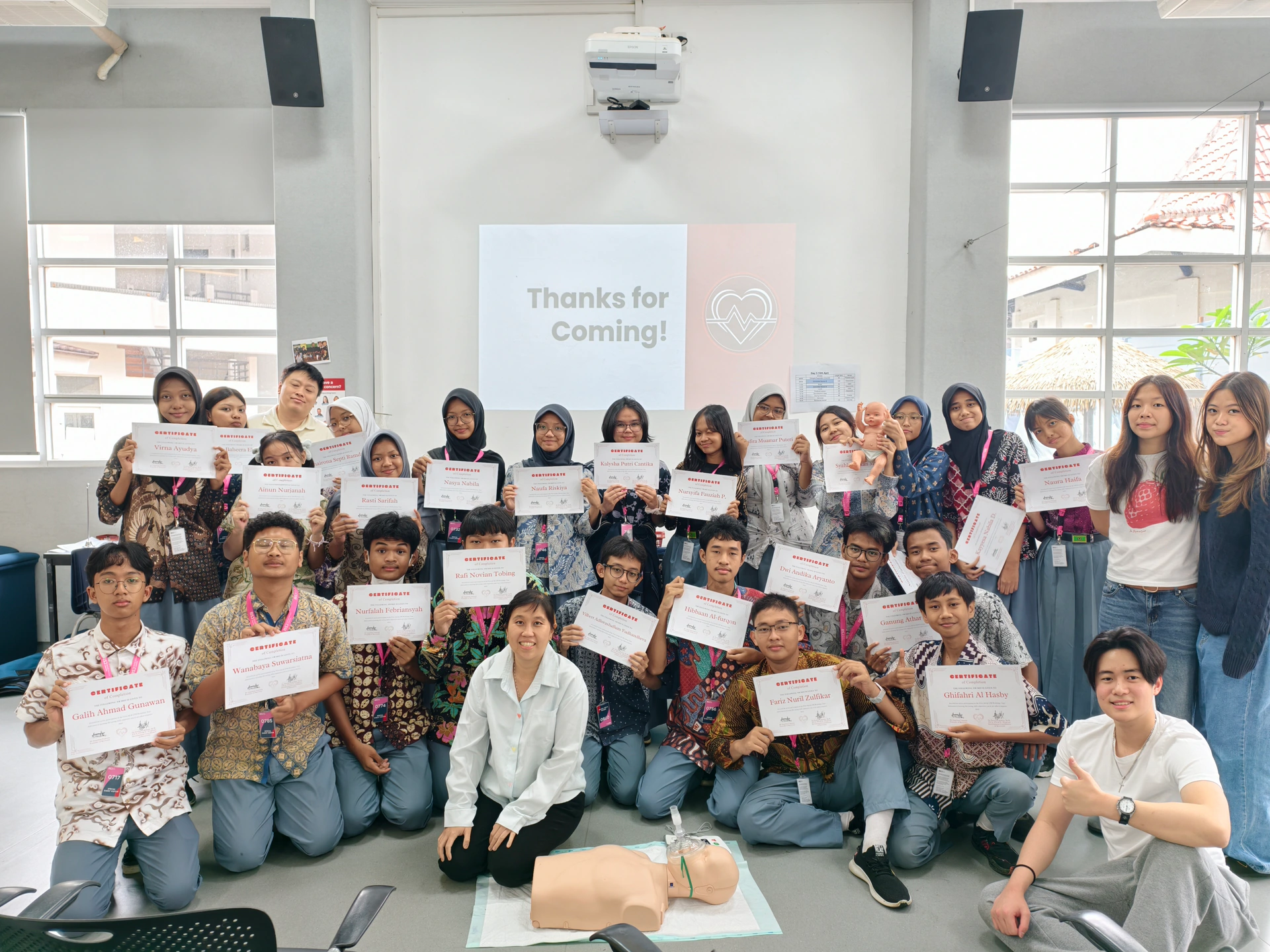 Beatkeepers workshop participants holding their certificates, gathered around CPR training manikins