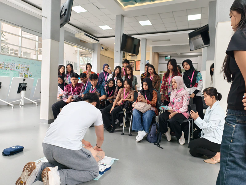 Students watch a Beatkeepers coach demonstrate CPR with a manikin and AED trainer