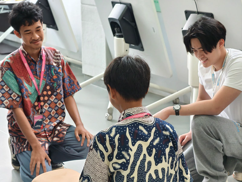 A smiling coach and students talk together beside a CPR training manikin