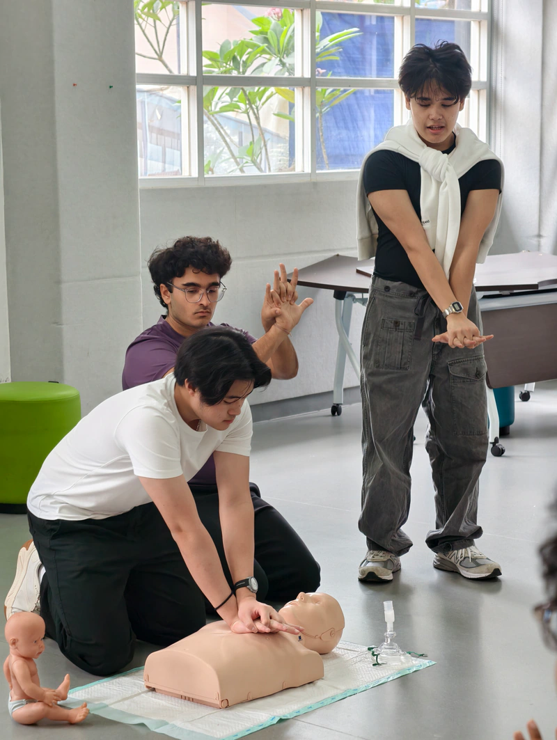 Three workshop coaches demonstrate hand placement and chest compressions on a CPR manikin