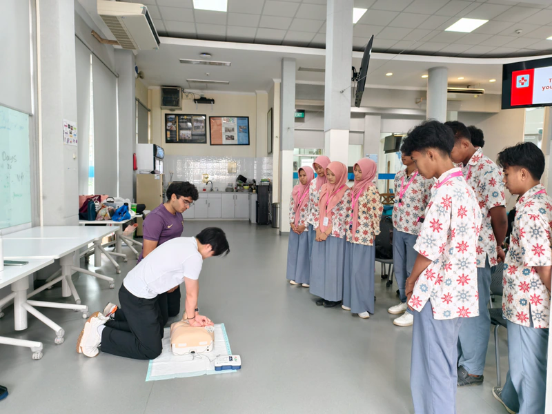 Students in school uniforms watch a chest compression demonstration