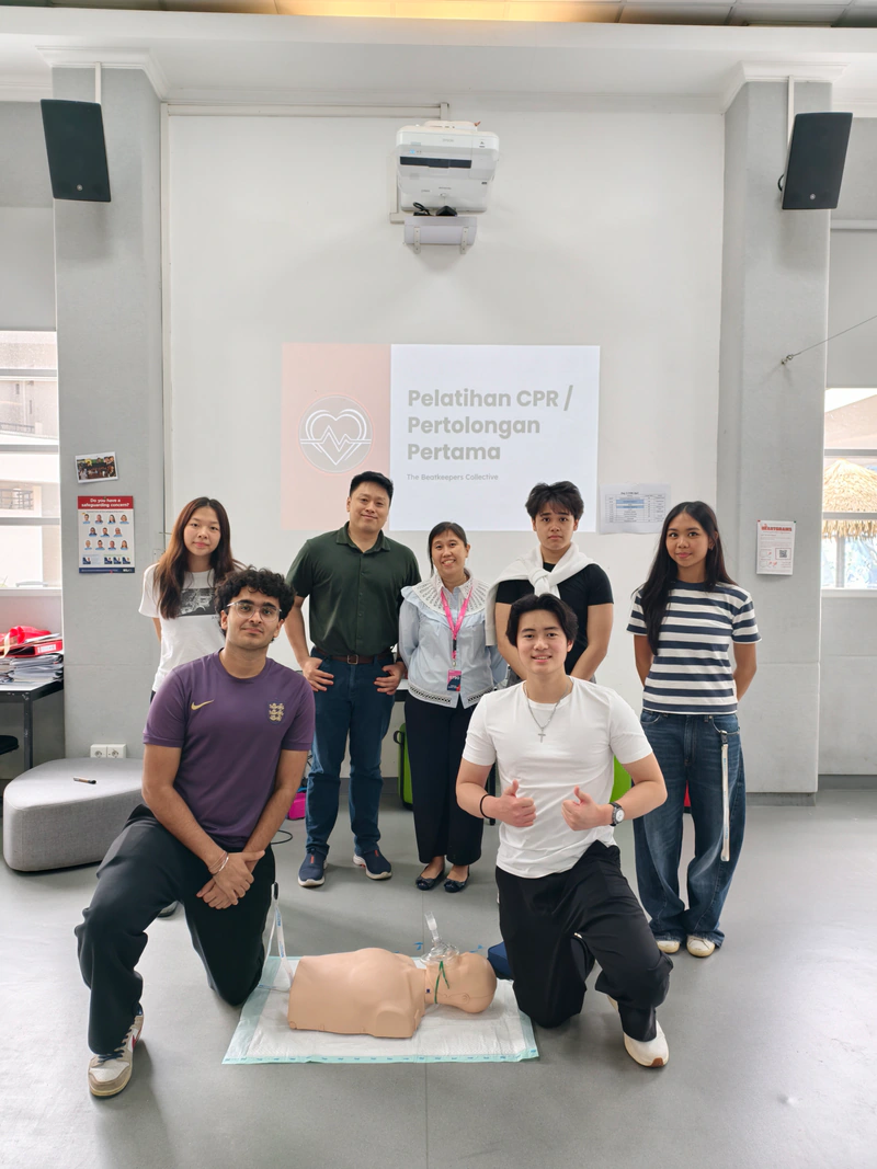Seven workshop team members pose together behind a CPR training manikin
